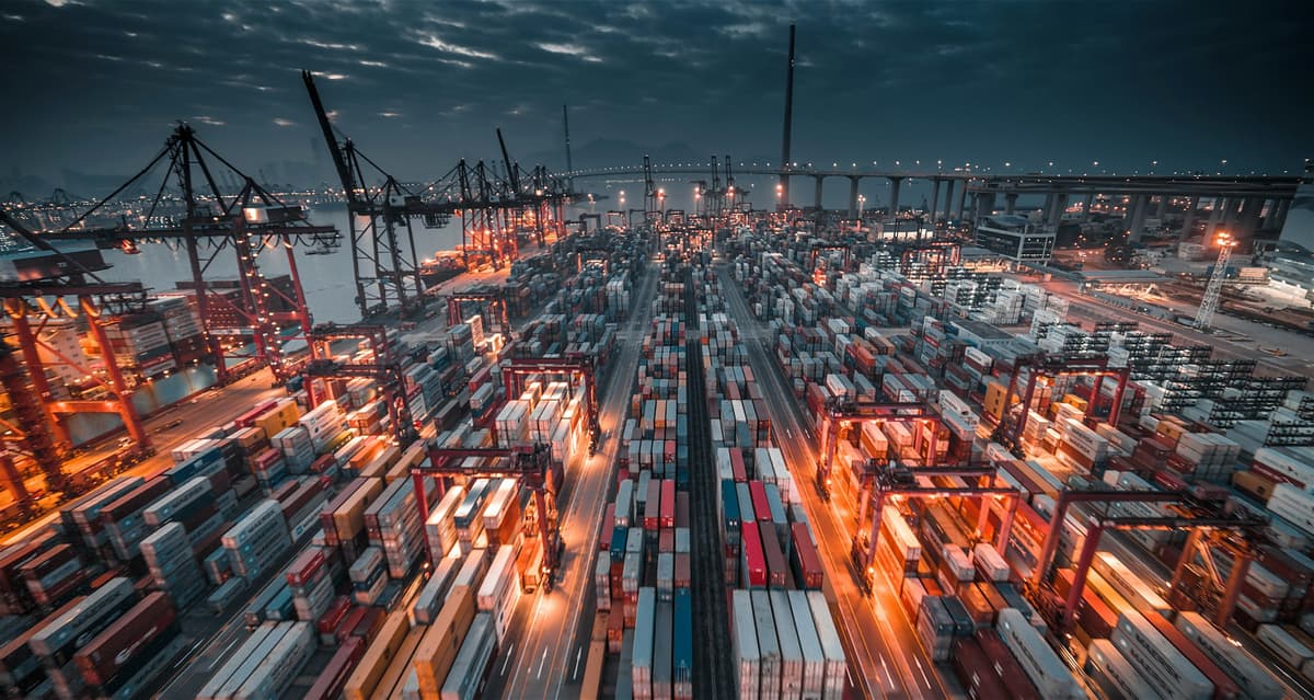 Aerial view of a container terminal lit up at night with cranes and stacked containers