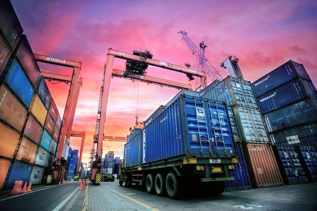 Container truck driving through a stacked container yard at sunset